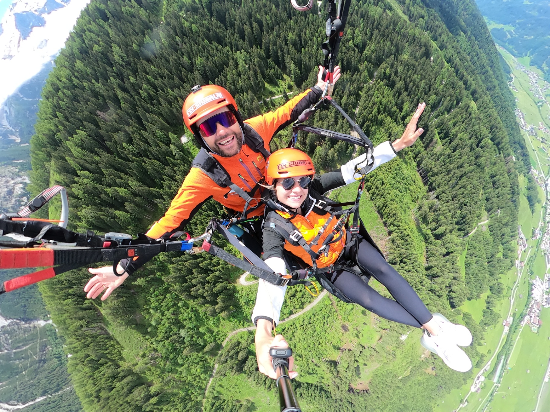 Lachender Gast und Pilot beim Tandem-Paragliding hoch über dem grünen Stubaital