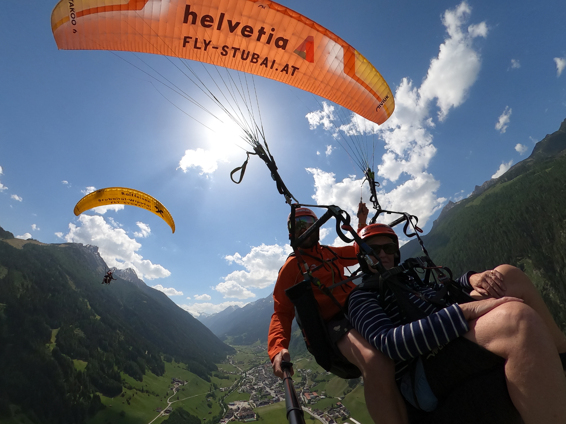 Tandemflug über dem Stubaital mit orangefarbenem Schirm und weitem Talblick nahe Innsbruck